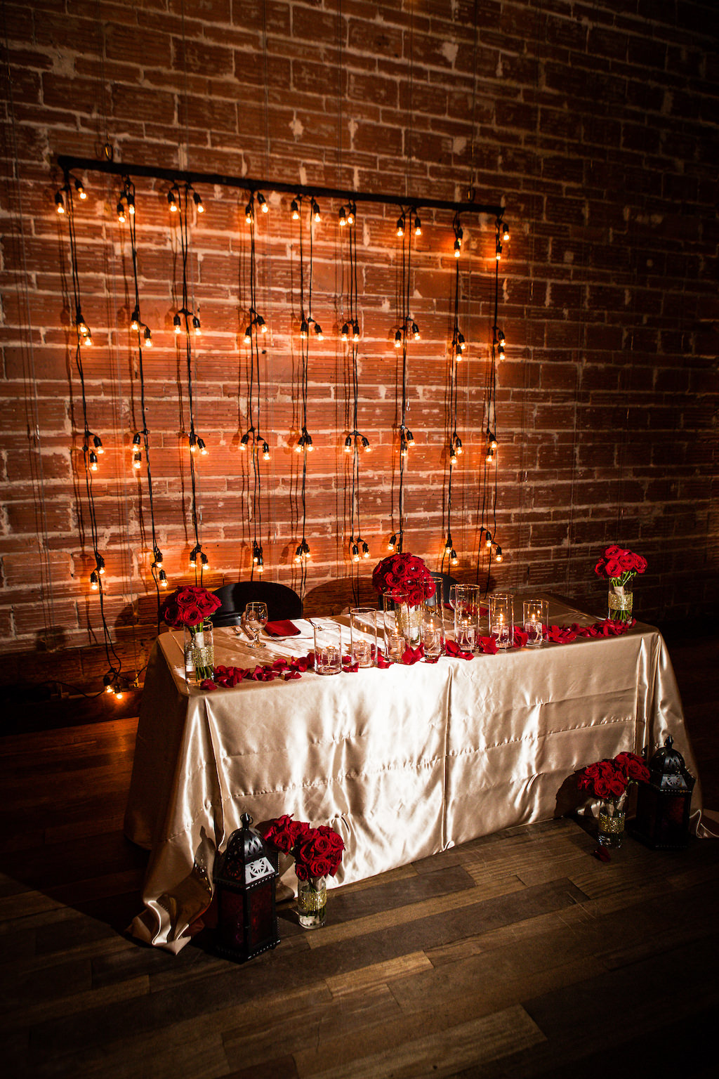 Great Gatsby Inspired Indoor Wedding Reception at St. Pete Venue and Sweetheart Table with Champagne Satin Linens, Red Roses Bouquets and Petals, Black Lantern and Bistro Light Backdrop | Downtown St. Pete Wedding Venue NOVA 535