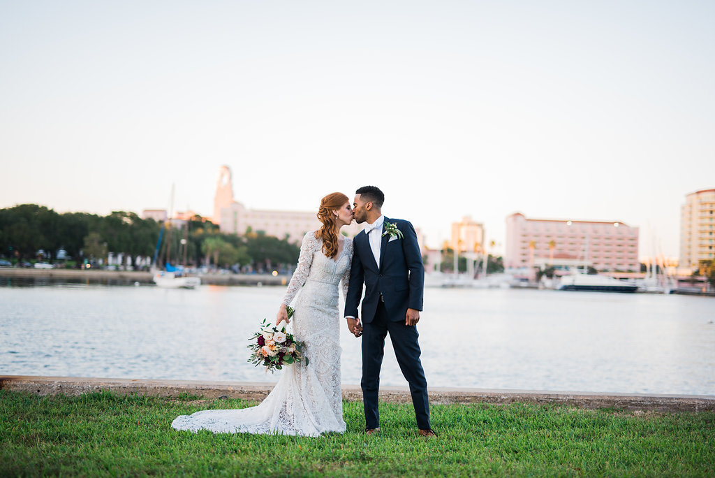 Waterfront Outdoor St. Petersburg North Straub Park Off-White Lace Long Sleeve Peek-A-Boo Back Vintage Inspired Bridal Portrait, with Blush Pink Roses and Greenery Organic Bouquet and Groom Wearing Navy Blue Tuxedo, Bow Tie and Organic Boutonniere | Downtown St. Pete Wedding Photographer Kera Photography
