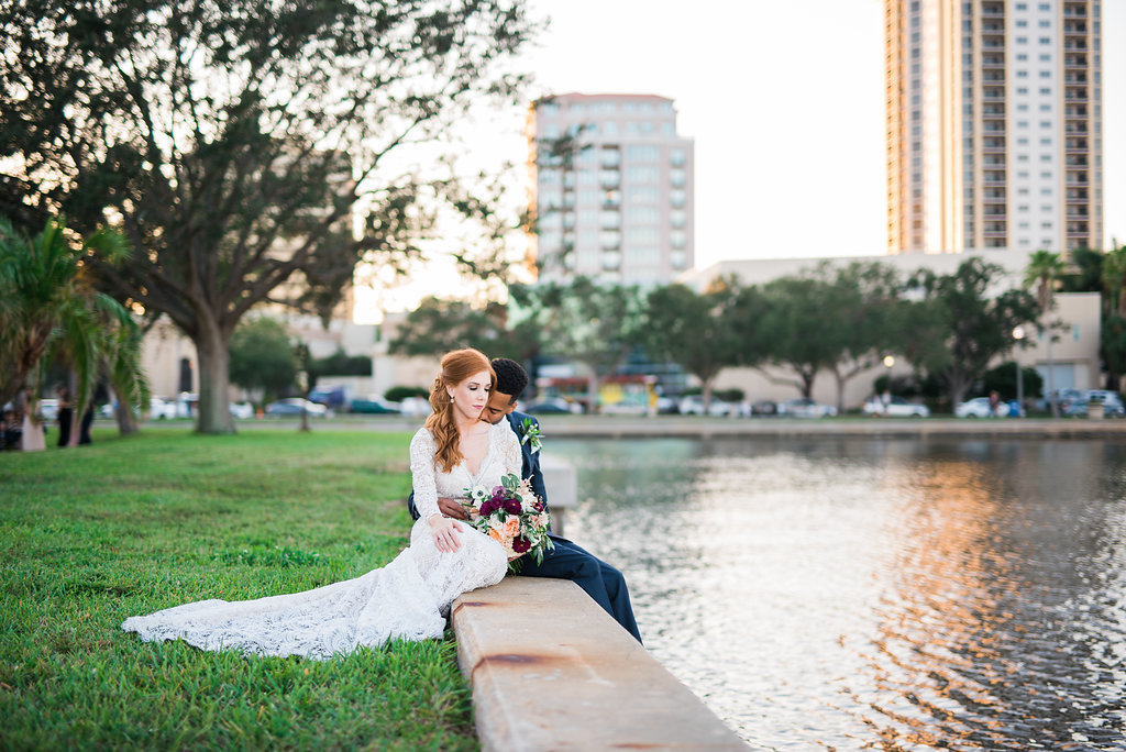 Waterfront Outdoor Off-White Lace Long Sleeve Peek-A-Boo Back Vintage Inspired Bridal Portrait at North Straub Park, with Blush Pink Roses and Greenery Organic Bouquet and Groom Wearing Navy Blue Tuxedo, Bow Tie and Organic Boutonniere | Downtown St. Pete Wedding Photographer Kera Photography