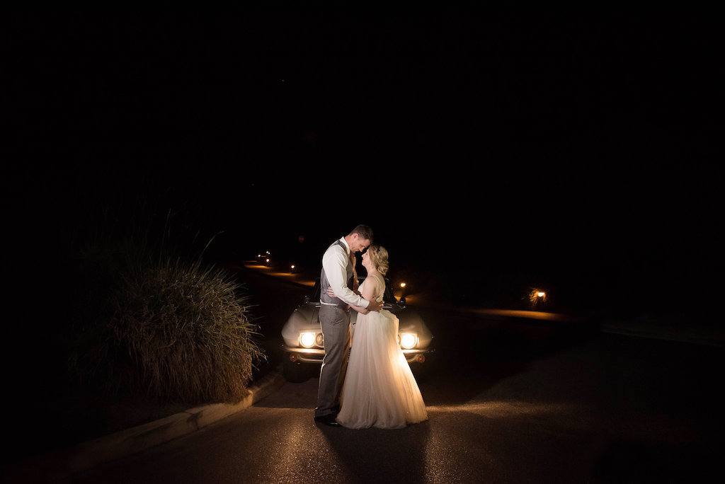 Outdoor Nighttime Bride and Groom Portrait in Front of White Vintage Car, Bride Wearing V-Neck Plunging Neckline with Floral Lace Overlay and Blush Pink Lining and Tank Straps, A-Line Tulle Skirt Wedding Dress, Teardrop Diamond Earrings, Braided Updo, Groom Wearing Light Grey Suit Vest with Dusty Blue Tie | Marry Me Tampa Bay Photographer Kristen Marie Photography | Marry Me Tampa Bay Hair and Makeup Destiny and Light Hair and Makeup Group