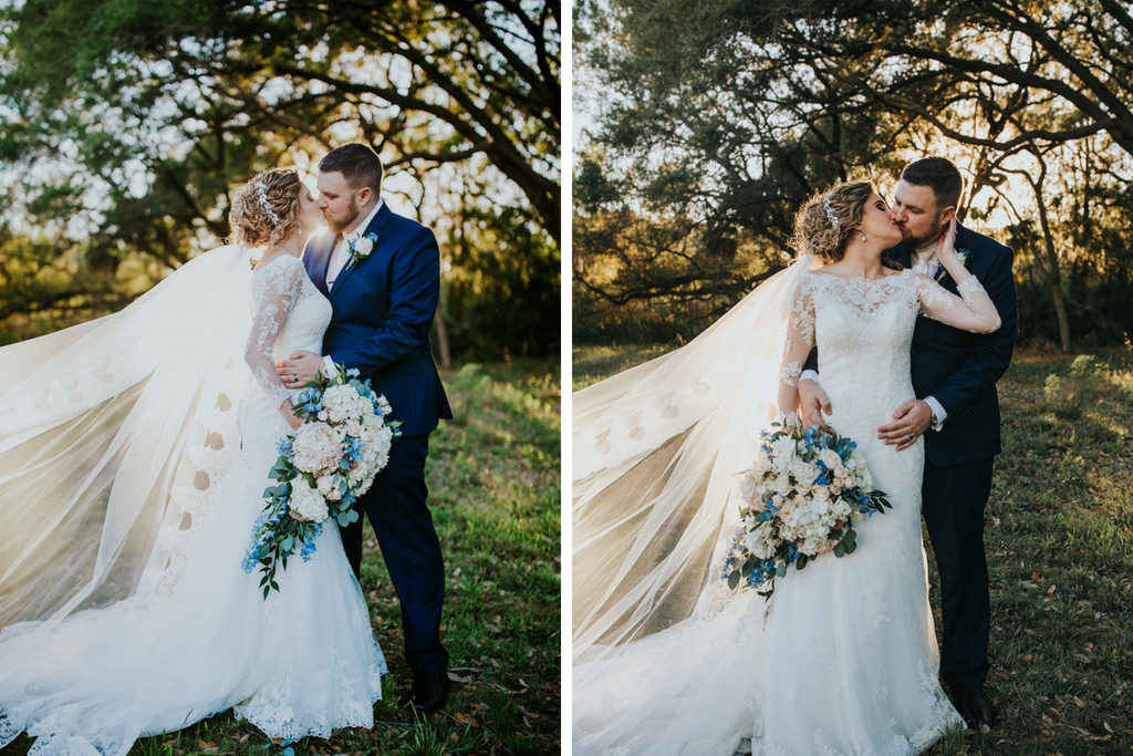 Outdoor Bride and Groom Sunset Wedding Portrait, Bride Wearing Long Sleeve Lace Mermaid Style Stella York Wedding Dress and Cathedral Length Lace and Tulle Veil Holding White, Blush, Blue Floral and Greenery Bouquet, Groom Wearing Navy Blue Suit with Blue Boutonniere | Safety Harbor Wedding Venue Harborside Chapel