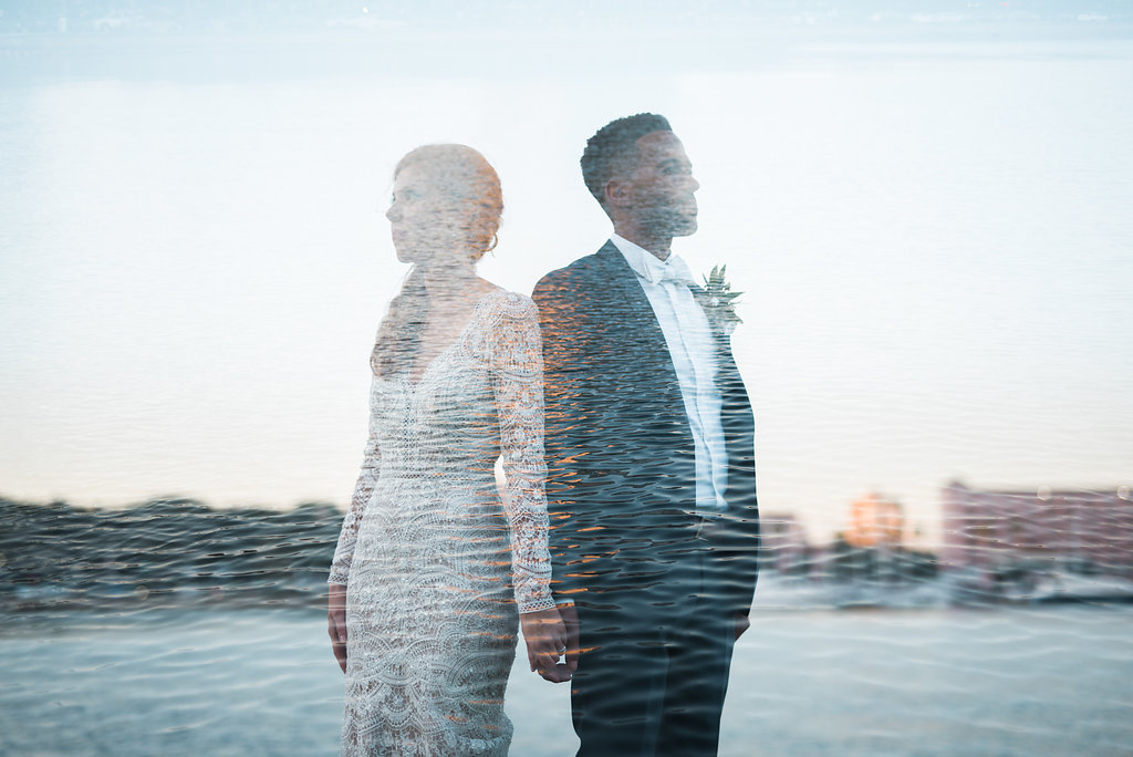 Waterfront Outdoor Off-White Lace Long Sleeve Peek-A-Boo Back Vintage Inspired Bridal Portrait, with Blush Pink Roses and Greenery Organic Bouquet and Groom Wearing Navy Blue Tuxedo, Bow Tie and Organic Boutonniere with Water Feature Overlay | Downtown St. Pete Wedding Photographer Kera Photography