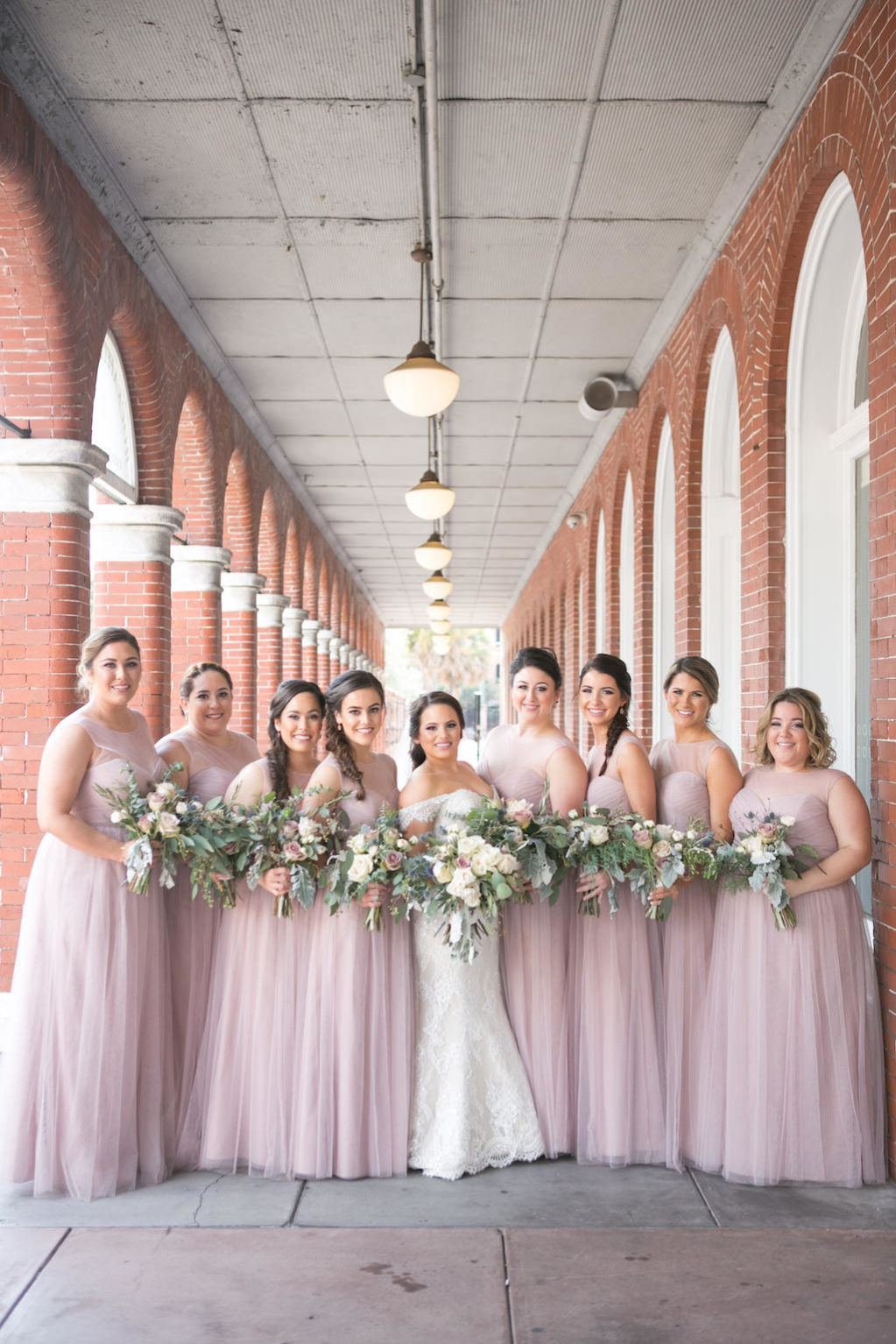 Outdoor Architectural Bridal Party Portrait, Bride in Off The Shoulder Lace Mermaid Augusta Jones Dress, Bridesmaids in Matching Strapless Layered Mauve Pink Jenny Yoo Dresses, with Blush Rose and Floral and Greenery Bouquet | Tampa Bay Wedding Photographer Carrie Wildes Photography | Dress Shop Bella Bridesmaids