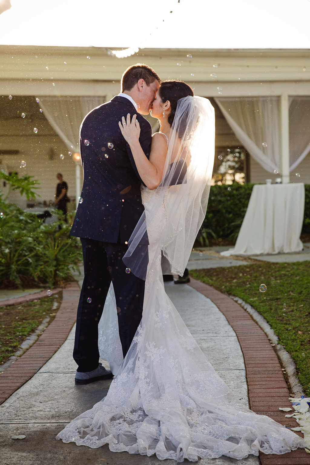 Outdoor Bride and Groom Portrait with Bride Wearing White Lace Wedding Dress and Veil and Groom Wearing Blue Tuxedo and Bubbles | Tampa Bay Wedding Photographer Marc Edwards Photographs