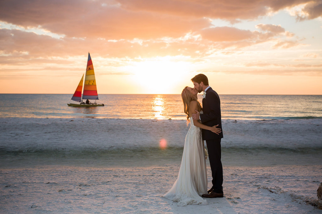Florida Bride and Groom Kissing During Sunset on Siesta Key Beach with Sailboat in Background Wedding Portrait | Photographer: Cat Pennenga Photography