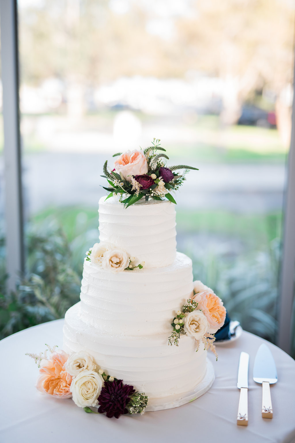 Three Tier Round White Wedding Cake with Ivory and Blush Roses, Burgundy Flowers and Greenery on Silver Plate with Floral Cake Topper | Naples Wedding Photographer Kera Photography | St. Pete Wedding Caterer Olympia Catering