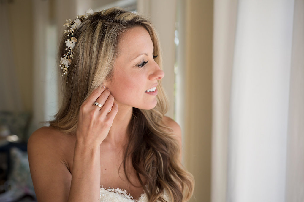 Bridal Portrait of Bride Putting on Earring with Hair Down and Wavy Wearing Flower Headpiece