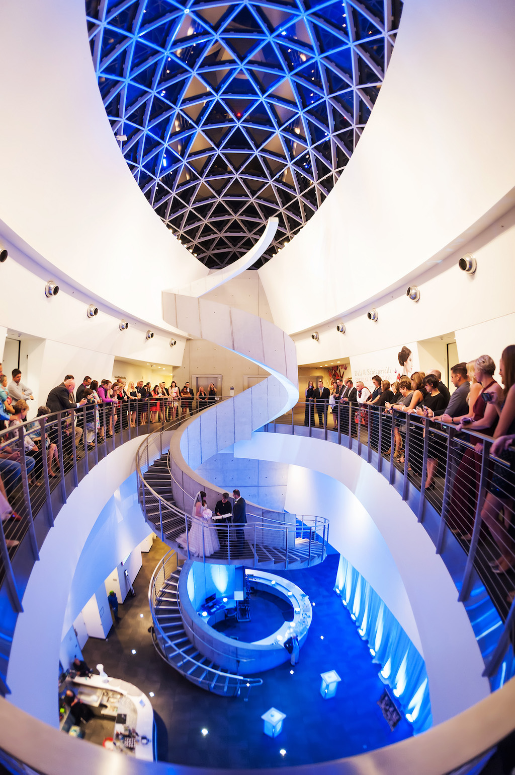 Salvador Dali Museum Ceremony Spiral White Staircase with Blue Uplighting and Bride and Groom Exchanging Vows with Guests Overlooking Balcony