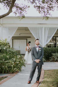 Bride and Groom First Look Portrait, Groom in Grey Tuxedo and Burgundy Bowtie with White Rose and Red Flower Boutonniere, Bride in Boho Chic V-Neck Lace Illusion White Wtoo Wedding Dress with White Floral and Greenery Bouquet | Tampa Bay Wedding Venue Davis Islands Garden Club