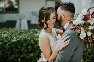 Bride and Groom First Look Portrait, Groom in Grey Tuxedo and Burgundy Bowtie with White Rose and Red Flower Boutonniere, Bride in Boho Chic V-Neck Lace Illusion White Wtoo Wedding Dress with White and Red Floral and Greenery Bouquet | Tampa Bay Wedding Venue Davis Islands Garden Club