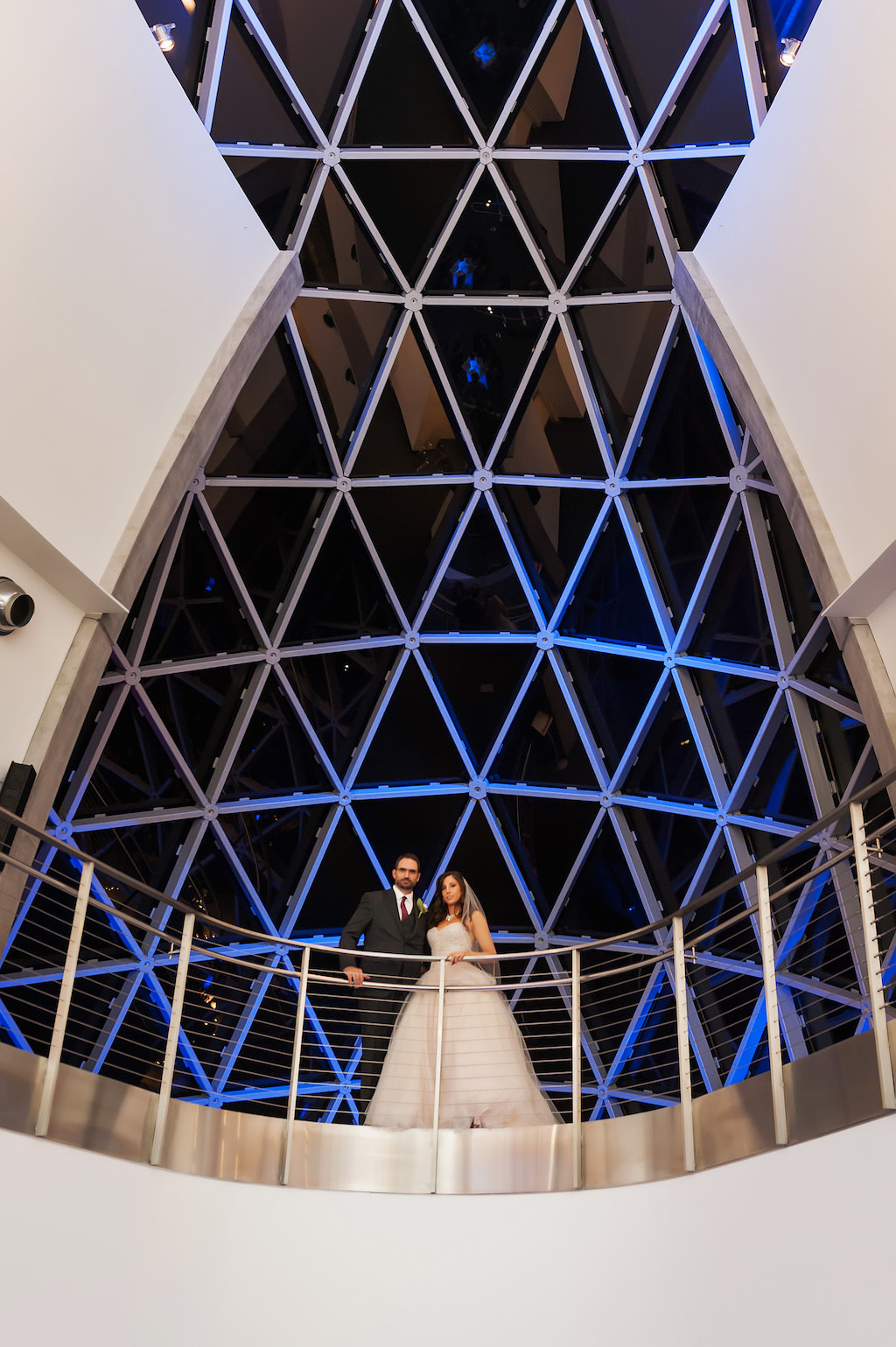 Bride and Groom Overlooking Balcony at Salvador Dali Museum with Triangular Window Backdrop and Blue Uplighting
