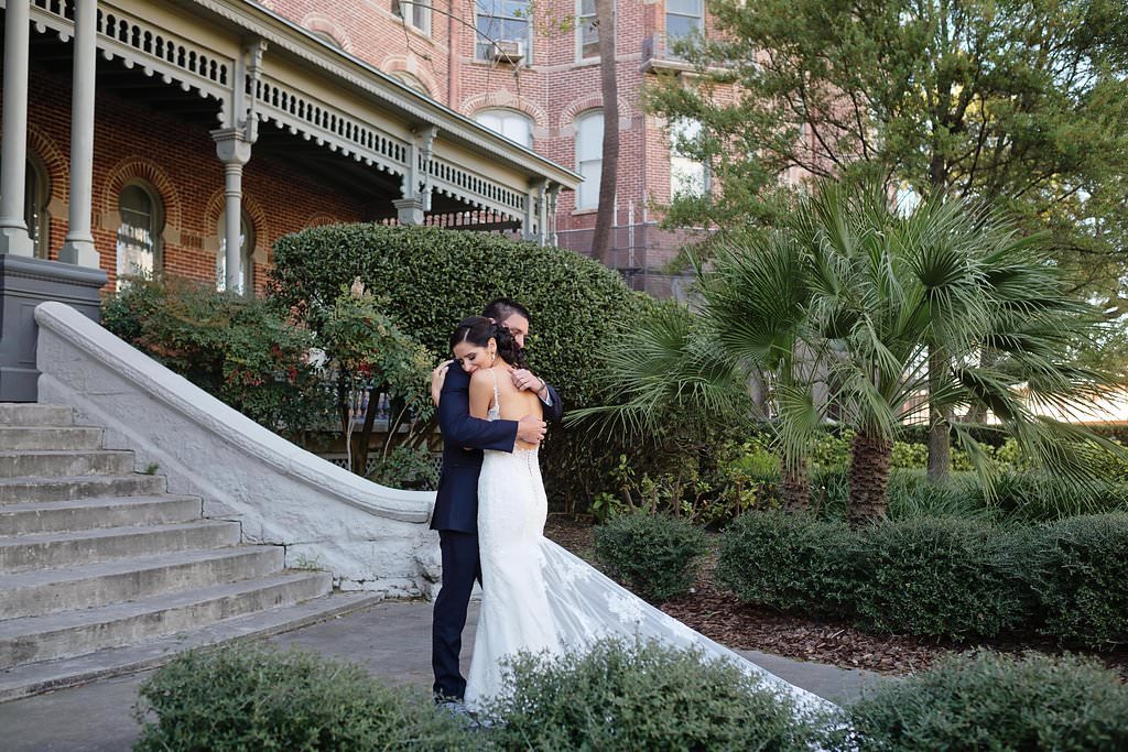 Outdoor University of Tampa Bride and Groom Wedding Portrait Groom Wearing Blue Tuxedo and Bride Wearing Low Back Strappy White Lace Wedding Dress with Lace Train | Tampa Bay Photographer Marc Edwards Photographs