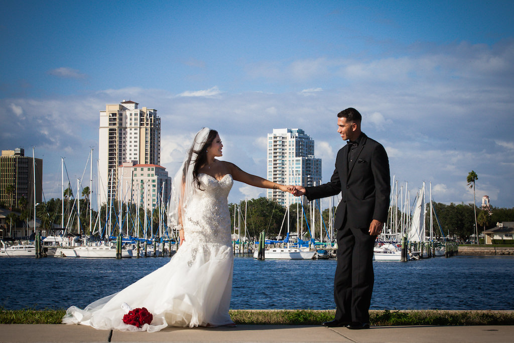 Outdoor Waterfront Wedding Bride and Groom Portrait with White Rhinestone Sweetheart Dress, Red Rose Bouquet, and Groom Wearing Black Tuxedo, Black Shirt and Black Tie