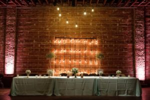 Bride and Groom Sweetheart Table with Glass Cylinders and Florals, Exposed Brick and Industrial String Lights, White Pedestals with Glass Cylinders and Baby's Breathe | Modern Industrial Wedding Reception Decor Inspiration | Downtown St. Petersburg Wedding Venue NOVA 535 | St. Pete Photographer Marc Edwards Photography