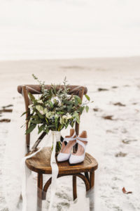 Wooden Ceremony Chairs with Greenery and White Flower Bouquet, White Pointed Shoes, Wedding Rings and Veil on Sandy White St. Pete Beach Wedding