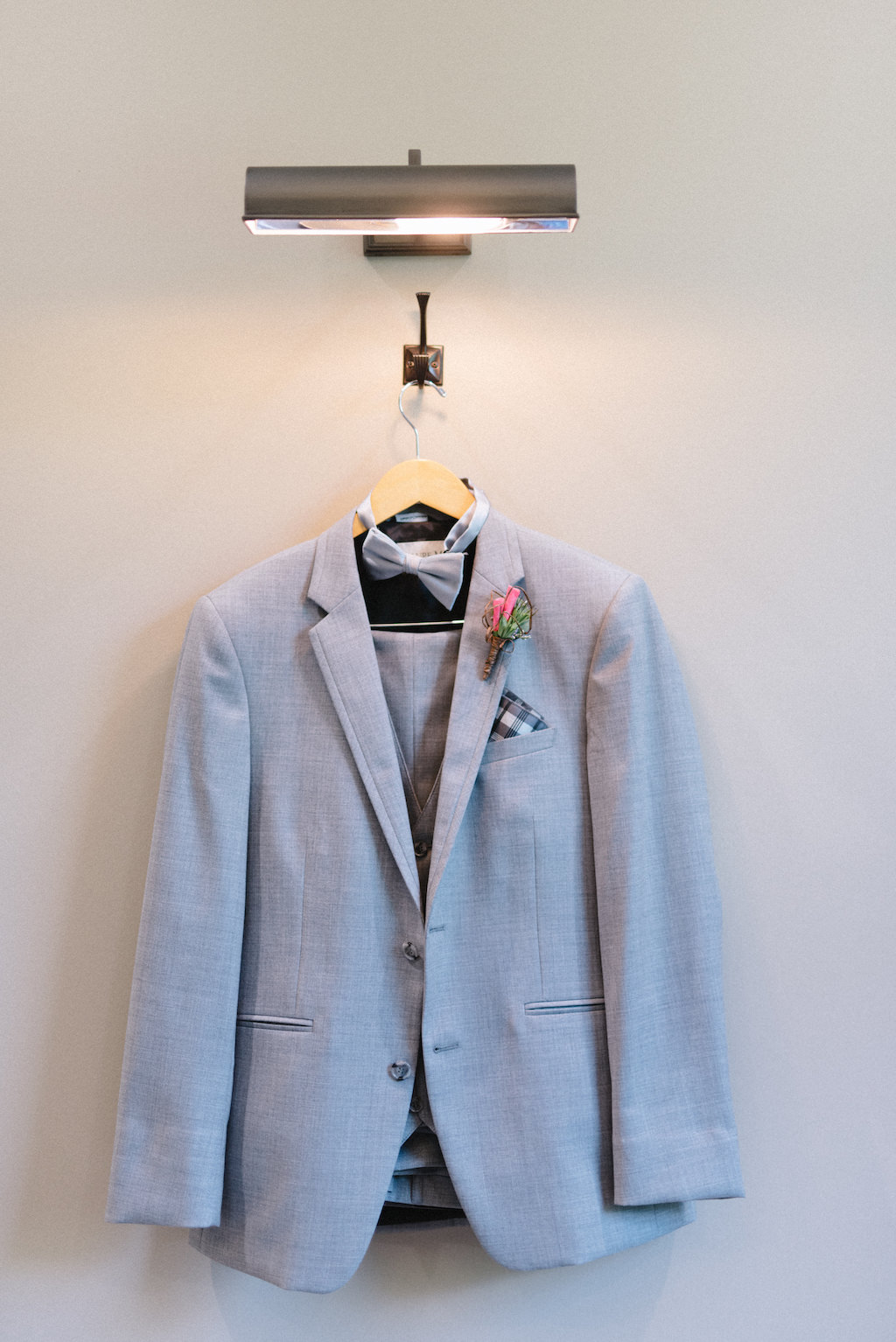 Men's Grey Suit and Bowtie with Checkered Handkerchief and Pink and Greenery Floral Boutonniere on Hanger | Groom Black Leather Dress Shoes, Pink Flower and Greenery Boutonniere | Naples Wedding Photographer Kera Photography | Nikki's Glitz and Glam Bridal Boutique | Clearwater Beach Wedding Photographer Kera Photography