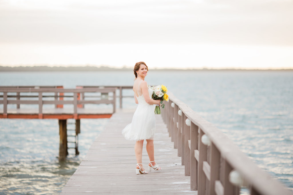 Outdoor Waterfront Bridal Wedding Portrait on Dock, Bride wearing White Spaghetti Strap Short Reception Wedding Dress with Yellow Sunflower, White Daisy and Greenery Floral Bouquet | Dunedin Wedding Venue Beso Del Sol Resort