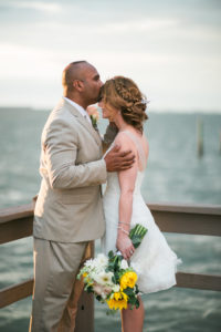 Intimate, Outdoor Waterfront Bride and Groom Wedding Portrait on Dock, Bride wearing White Tank Top Strap Short Reception Wedding Dress with Yellow Sunflower, White Daisy and Greenery Floral Bouquet and Braid, Groom in Tan Suit and Blush Pink Rose Boutonniere | Dunedin Wedding Venue Beso Del Sol Resort