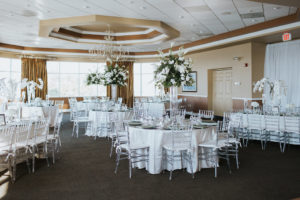 Romantic Ballroom Wedding Reception Decor with Tall White Orchid Floral and Natural Greenery Centerpiece in Glass Cylinder Vase, Round Tables with Clear Acrylic Chiavari Chairs and White Tablecloth and Green Linens | St. Pete Wedding Venue Isla Del Sol Yacht and Country Club | Tampa Bay Rentals Over The Top Linen Rentals and Gabro Event Rentals
