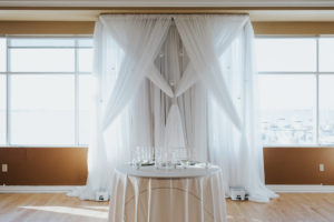 Indoor Ballroom Wedding Reception Sweetheart Table with White Linen and Decorative Silver Hanging Balls Backdrop, White Acrylic Chiavari Chairs, Off-White Tablecloth | St. Pete Wedding Venue Isla Del Sol Yacht and Country Club | Wedding Rentals Over the Top Linen Rentals and Gabro Event Rentals