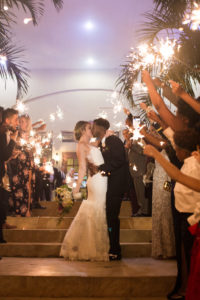 Outdoor Bride and Groom Sparkler Exit Portrait with Wedding Guests, Bride Wearing Spaghetti Strap Lace V-Neck Mermaid Wedding Dress, Updo, White, Deep Purple and Greenery Flower Bouquet, Groom Wearing Black Tuxedo | Clearwater Beach Wedding Venue Feather Sound Country Club