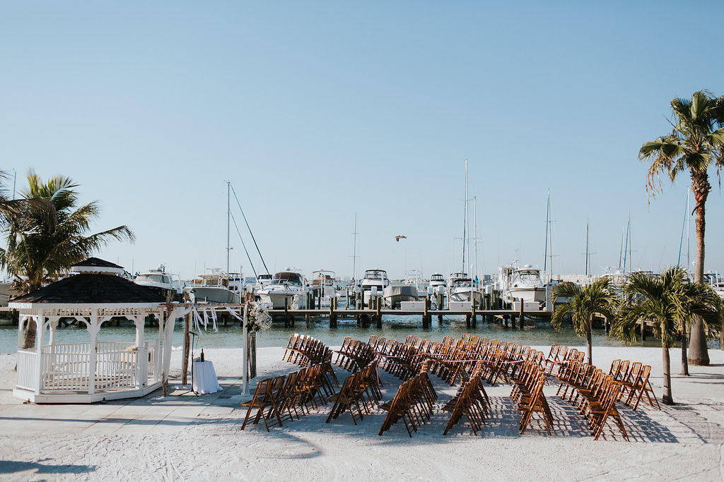 Outdoor Waterfront Beach Wedding Ceremony with Wedding Arch with White Draping and Wooden Ceremony Chairs | Tampa Bay Wedding Venue Isla Del Sol Yacht and Country Club
