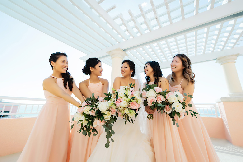 Outdoor Waterfront Hotel Rooftop Bridesmaids Portrait, Bride in Strapless White Trumpet Organza Wedding Dress and Rhinestone Belt with Veil and Blush, Ivory Rose and Greenery Bouquet, Bridesmaids in Mismatched Blush Pink Dresses with Ivory and Pink Roses and Greenery Bouquets | Venue Hyatt Regency Clearwater Beach