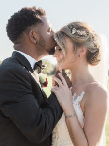 Intimate Outdoor Wedding Portrait, Bride in Spaghetti Strap Lace Dress, Curled Hair Updo with Floral Headpiece and Tulle Veil, Groom in Black Tuxedo with White Rose and Red Flower Boutonniere | Tampa Bay Wedding Hair and Makeup Artist LDM Beauty Group