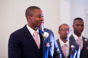 Groom's Reaction to Bride Walking Down the Aisle Wedding Ceremony Portrait in Navy Blue Suits, Blush Pink Ties, and White Rose Boutonniere