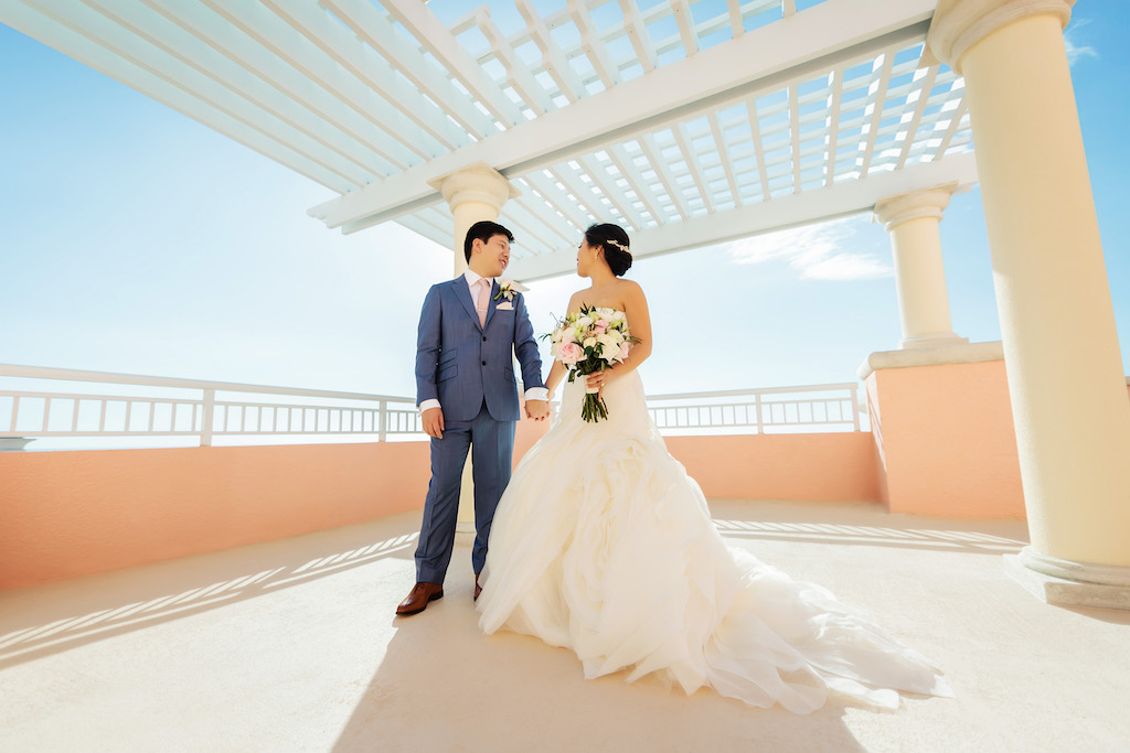 Outdoor Waterfront Hotel Rooftop Bride and Groom Portrait, Bride in Strapless White Trumpet Organza Wedding Dress and Rhinestone Belt with Veil and Blush, Ivory and Greenery Floral Bouquet, Groom in Blue Suit with Blush Pink Tie and Blush and Ivory Rose Boutonniere | Venue Hyatt Regency Clearwater Beach