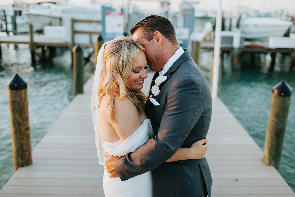 Romantic, Waterfront Bride and Groom Wedding Portrait, Bride in Mikaella Off the Shoulder, Sweetheart Wedding Dress and Tulle Veil, Groom in Grey Suit and White Cala Lillie Boutonniere | St. Pete Beach Wedding Venue Isla Del Sol Yacht and Country Club