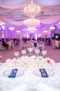 Indoor Wedding Reception Sweetheart Table Decor with White and Blush Pink Roses Centerpiece and Crystal Candle Holders, Clear Beaded Chargers, White Roses Tablecloth and White Draping and Chandeliers with Pink Uplighting | Tampa Bay Wedding Venue The Crystal Ballroom