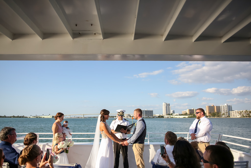 Outdoor On the Waterfront Wedding Ceremony Portrait, Bride in Beaded Bodice and White Chiffon Floor Length Wedding Dress and Cathedral Veil, Groom Wearing Khaki Pants, Blue and White Checkered Dress Shirt and Navy Blue Vest, Bridesmaid in Blush Pink Dress and Groom in Khaki Pants, White Dress Shirt and Navy Blue Tie, Flower Girl Holding White and Pink Floral Bouquets | Clearwater Beach Nautical Wedding Venue Yacht StarShip | Tampa Bay Wedding Photographer Lifelong Photography Studios