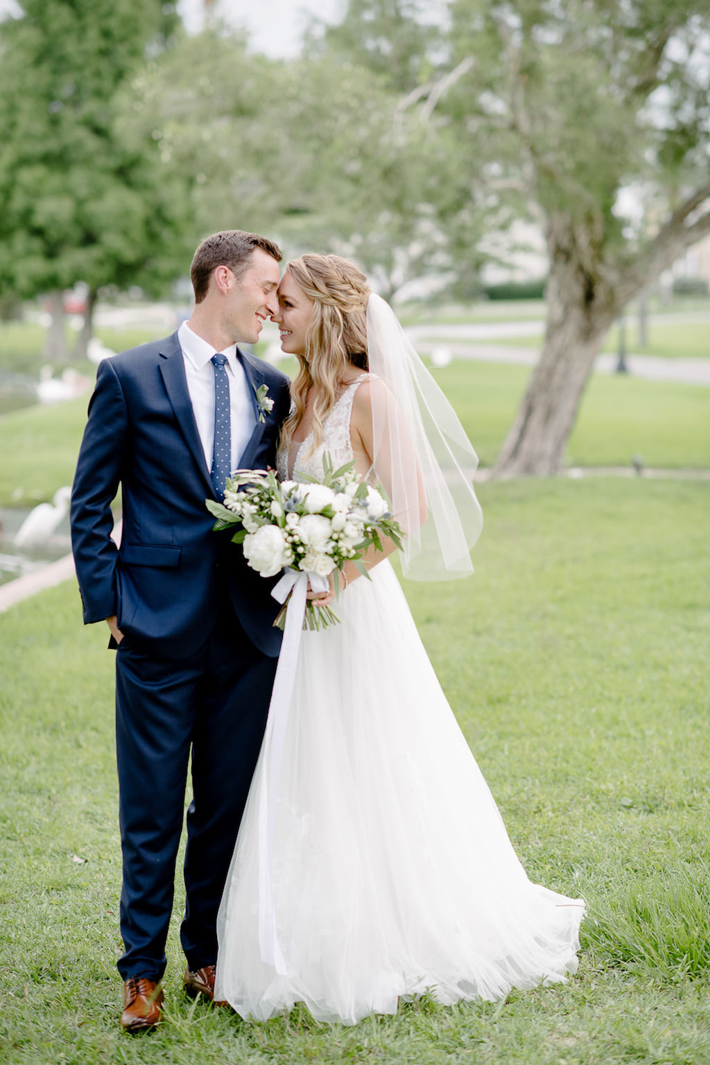 Outdoor Bride and Groom First Look Wedding Portrait, Groom in Navy Blue Suit and White Floral Boutonniere, Bride in White A-Line Illusion Tank Top Strap Plunging V-Neckline and Lace Bodice Wedding Dress with White Floral and Greenery Bouquet and Braided Half-Updo