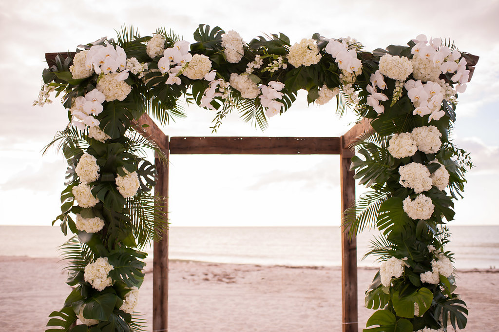 Outdoor Tropical Beach Wedding Ceremony Decor with Wooden Arch, Banana Leafs, White Hydrangeas and Orchids Wedding Planner Parties A La Carte | Clearwater Beach Wedding Venue Carlouel Yacht Club