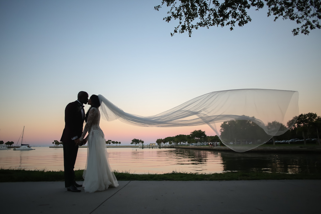 Creative Outside Waterfront Dark Sunset Bride and Groom Wedding Portrait with Veil Blowing in Wind | St. Petersburg Photographer Lifelong Photography Studios