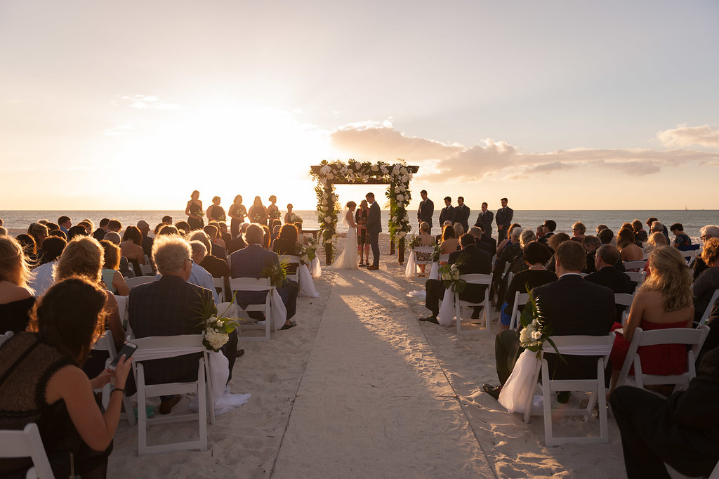 Clearwater Beach Wedding Ceremony Portrait with White Folding Chairs, Decorated with White and Greenery Floral Bouquets with Tulle, Ceremony Arch with White and Greenery Floral Wooden Arch |Tampa Wedding Planner Parties A La Carte | Wedding Venue Clearwater Beach Wedding Ceremony Portrait of Bride and Father Walking Down the Aisle, White Folding Chairs with White and Greenery Bouquets and Tulle and Ceremony Arch | Tampa Wedding Planner Parties A La Carte | Tampa Bay Wedding Rentals A Chair Affair | Clearwater Wedding Venue Outdoor Tropical Beach Wedding Ceremony Decor with Wooden Arch, Banana Leafs, White Hydrangeas and Orchids Wedding Planner Parties A La Carte | Clearwater Beach Wedding Venue Carlouel Yacht Club | Tampa Bay Rental Company A Chair Affair