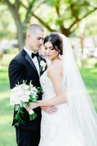 Outdoor Bride and Groom Wedding Portrait, Bride in Lace and Rhinestone High Neck Halter Fit and Flare Wedding Dress, Cathedral Length Veil, White and Greenery Bouquet, Groom in Black Tuxedo and White Rose Boutonniere | Tampa Wedding Photographer Ailyn La Torre | St. Petersburg Hair Artist Femme Akoi