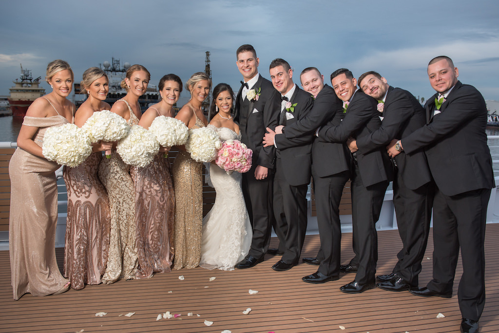 Outdoor Waterfront Bridal Party Portrait, Bridesmaids in Gold, Rose Gold Sequin Mismatched Dresses and White Floral Bouquet, Bride in Lace Off the Shoulder Wedding Dress with Pink and White Rose Bouquet, Groom and Groomsmen in Black Tuxedos with Floral Boutonniere | Downtown Tampa Nautical Wedding Venue Yacht StarShip