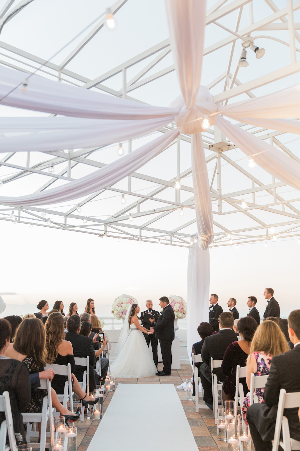 St. Pete Beach Wedding Ceremony Portrait with White Folding Chairs, Glass Cylinders with Floating Candles, White Runner and White Draping | St. Pete Beach Wedding Venue The Don Cesar