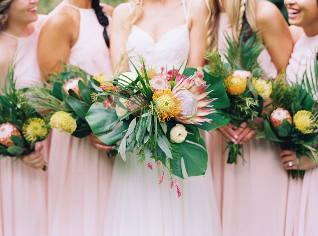 Outdoor Bride and Bridesmaid Portrait in Long Blush Pink Matching Dresses, Bride in Strappy V-neck Lace Wedding Dress with Tropical Pink, Yellow and Greenery Bouquets | St. Pete Wedding Planner Southern Glam Events and Weddings