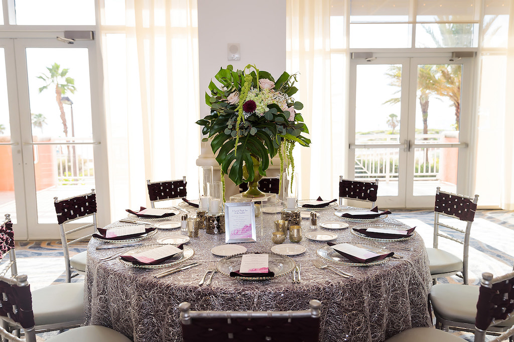 Elegant Ballroom Wedding Reception Decor, Silver Tablecloth, Tall Gold Vase on Clear Acrylic Stand, Blush Pink Roses, Amaranthus, and Tropical Palm Leaf Centerpiece, Clear and Silver Beaded Chargers, Silver Frames, Custom Menus, Silver Chiavari Chairs with Woven Plum Purple Chair Sash and Candlesticks | Wedding Venue Hyatt Regency Clearwater Beach | Tampa Bay Stationary A&P Designs | Over the Top Rental Linens