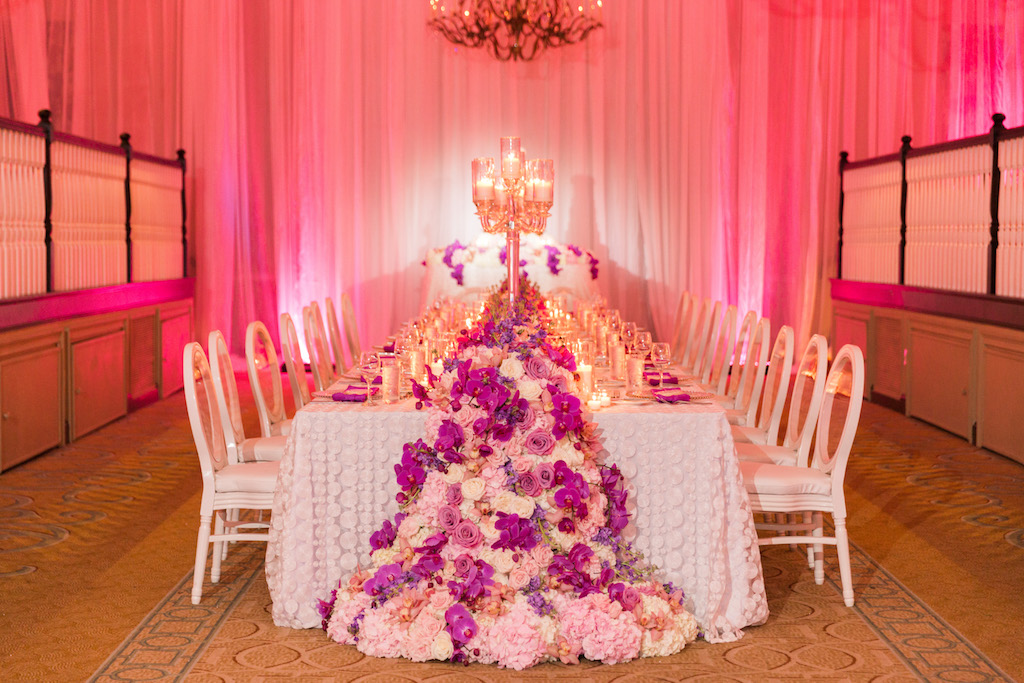 Elegant Ballroom Reception Decor, Long Feasting Table with Decorative White Linen, Fuchsia, Pink and White Floral Garland, Tall Candlestick and White Chairs and Pink Uplighting and Linen Draping | St. Pete Beach Historic Wedding Venue The Don Cesar