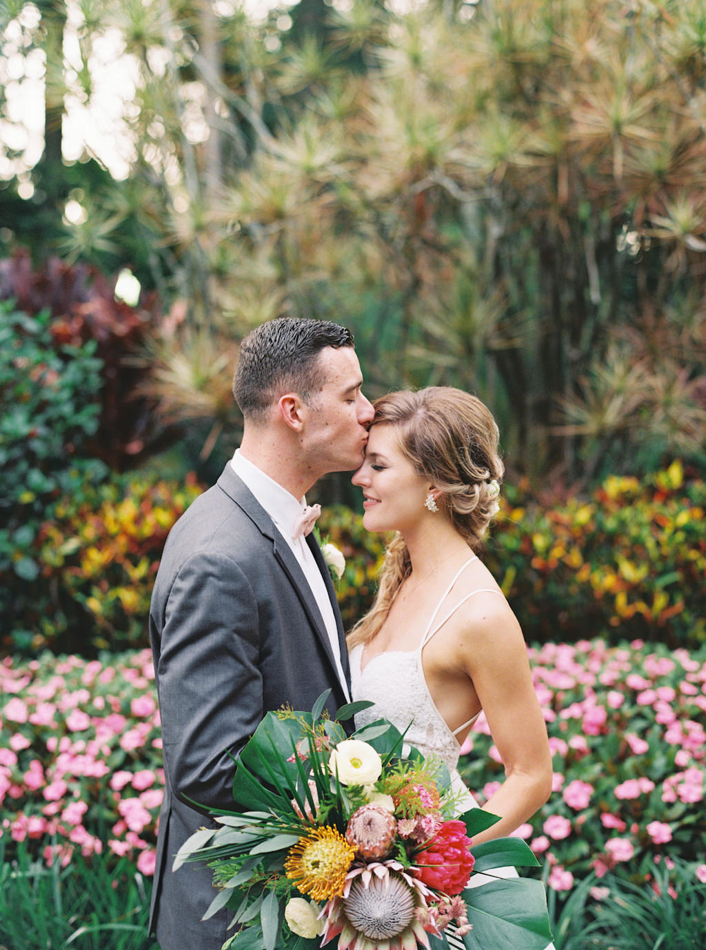 Outdoor Bride and Groom Portrait A-Line Strappy Lace Wedding Dress, Braided Hair with White Flowers and Greenery, White, Pink King Protea and Yellow Tropical Inspired Floral Bouquet, Groom in Grey Suit | Outdoor St. Petersburg Wedding Venue Sunken Gardens | Planner Southern Glam Events and Weddings