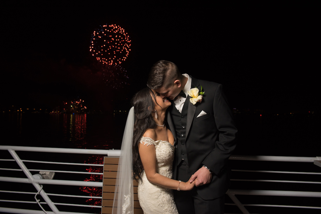 Outdoor Waterfront Nighttime and Fireworks Wedding Bride and Groom Portrait, Bride with Lace Off the Shoulder Wedding Dress and Veil, Groom in Black Tuxedo and Rose Boutonniere | Tampa Bay Nautical Wedding Venue Yacht StarShip