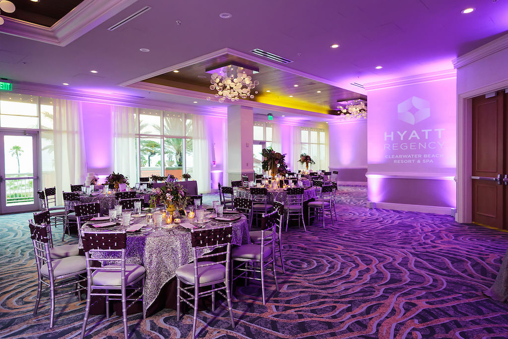 Elegant Ballroom Wedding Ceremony Reception Decor, Purple Uplighting, Wedding Venue Hyatt Regency Clearwater Beach Projected Sign, Round Tables with Silver Tablecloths, Silver Chiavari Chairs with Plum Woven Chair Sash | Tampa Bay Rentals Over the Top Linens