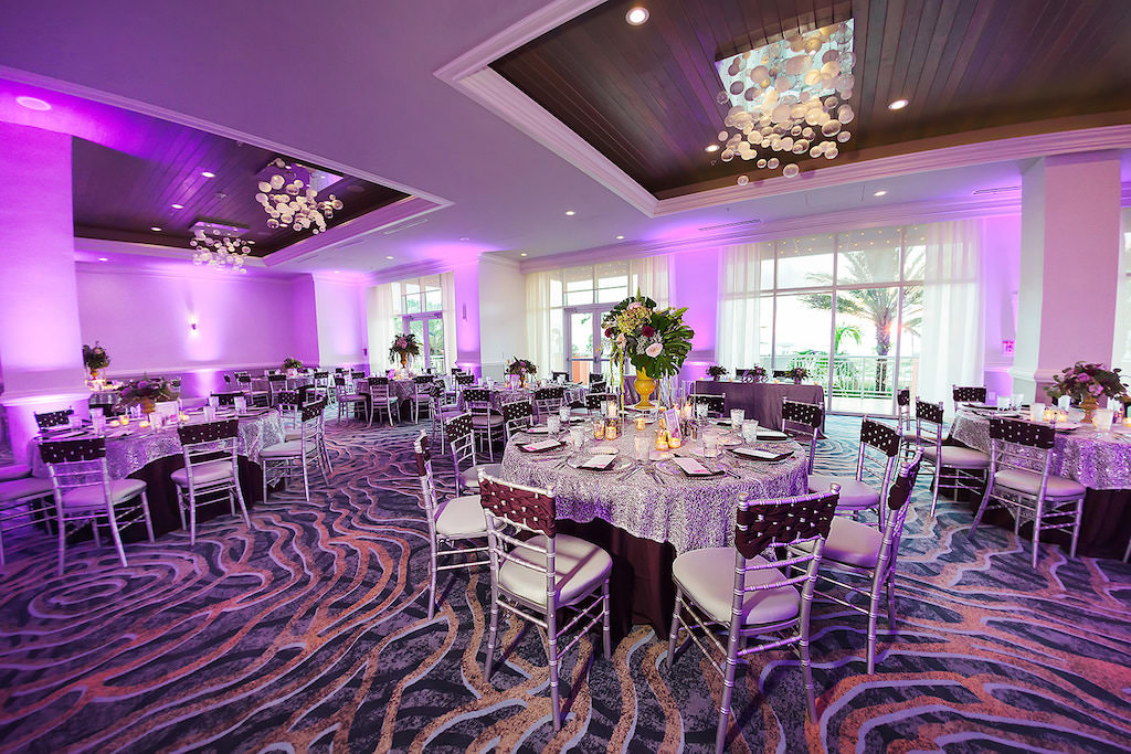 Elegant Ballroom Wedding Ceremony Reception Decor, Purple Uplighting, Round Tables with Silver and Dark Purple Tablecloths, Silver Chiavari Chairs with Plum Woven Chair Sash and Tall Gold Vase, Floral and Greenery Bouquet | Tampa Bay Rentals Over the Top Linens | Wedding Venue Hyatt Regency Clearwater Beach