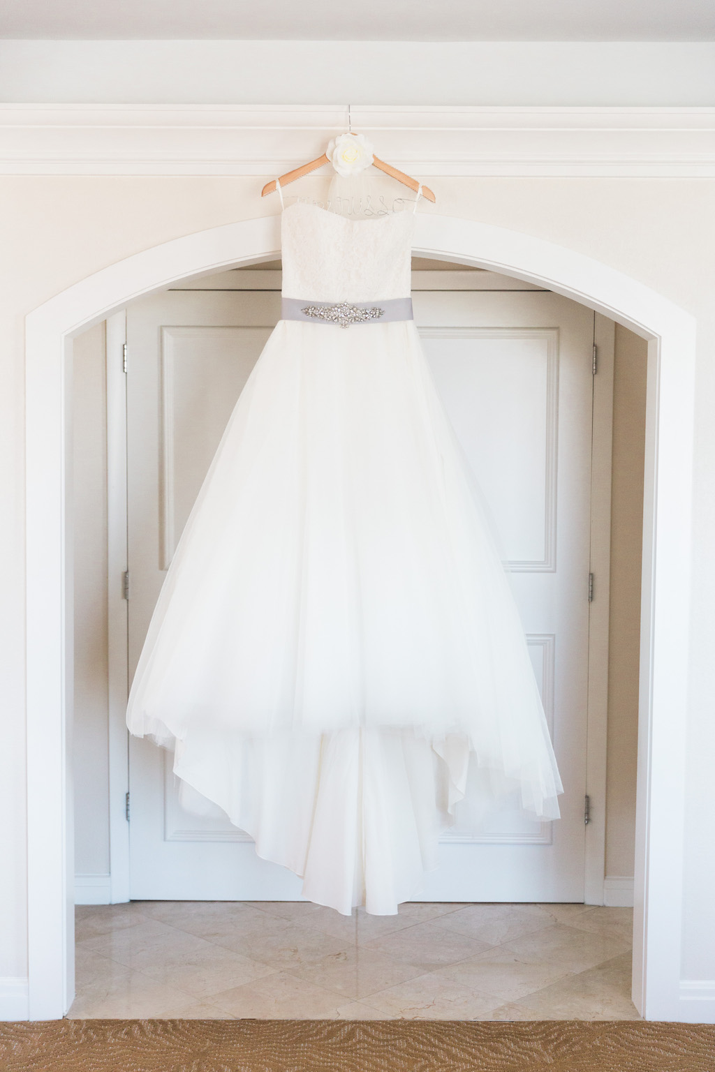 Strapless Scoop Neck Ballgown Wedding Dress with Grey Sash and Rhinestone Brooch on Wooden Hanger with White Rose Decor