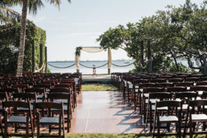 Waterfront Wedding Ceremony, Brown Wooden Folding Chairs, Arch with White Draping and Greenery and White Floral Bouquet | Sarasota Wedding Planner Kelly Kennedy Weddings and Events