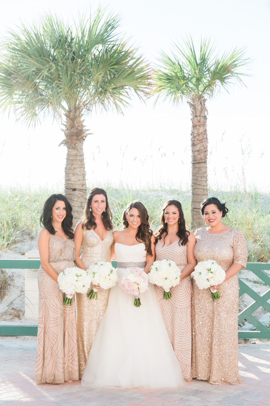 Outdoor St. Pete Beach Bridal Party Portrait, Bridesmaids in Gold Sequin Mismatched Dresses, Bride in Strapless Scoop Neck Ballgown Wedding Dress with Grey Sash and Pink and White Floral Bouquet